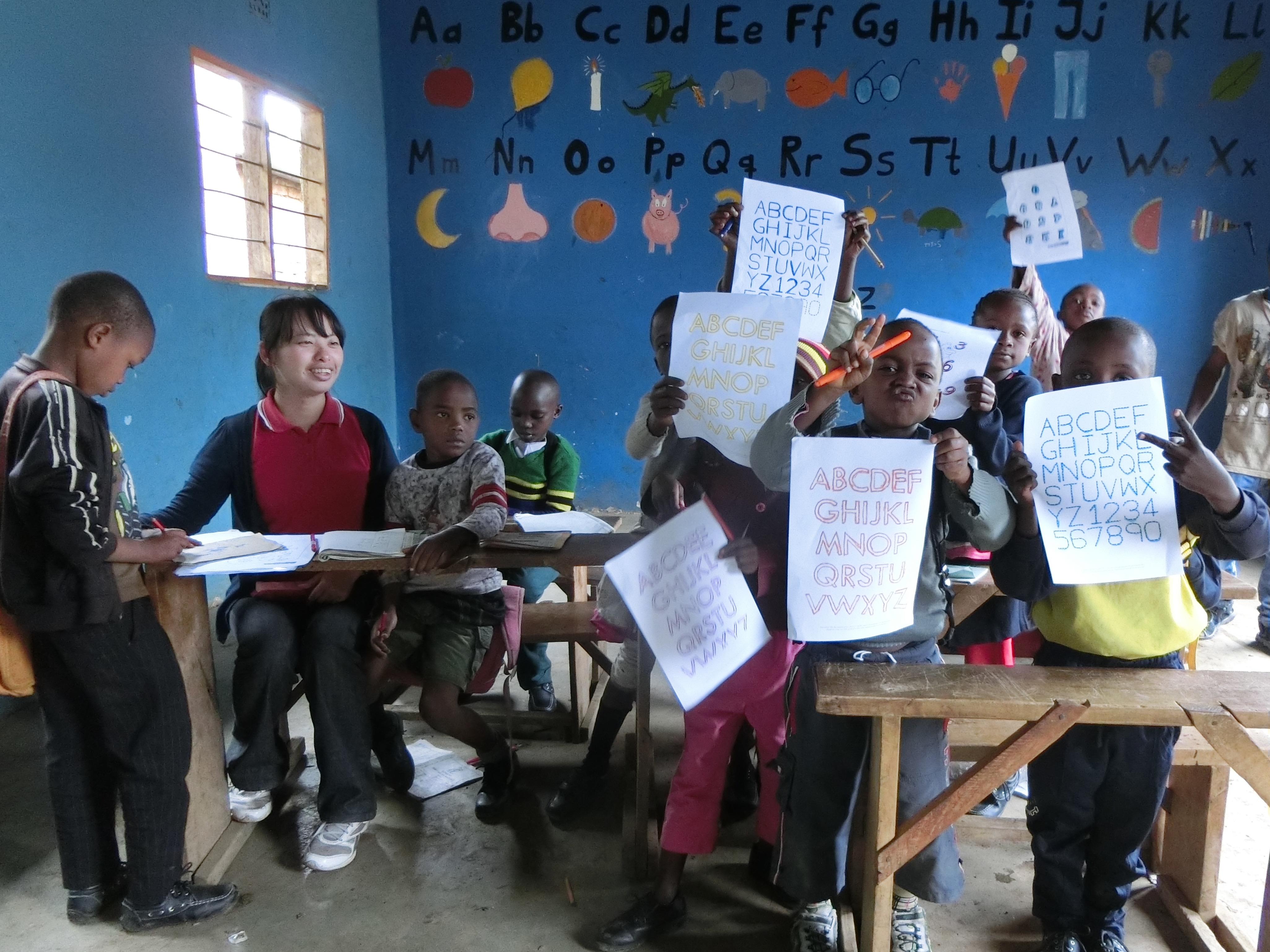Voluntaria enseñando inglés en Tanzania sonriendo al ver los ejercicios de sus alumnos. Pequeños estudiantes de Tanzania muestran sus ejercicios de inglés durante nuestro voluntariado de enseñanza.